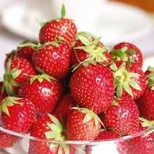 Red strawberries with green leaves in a bowl