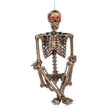 Gold-tone skeleton decoration with glowing red eyes, seated hands crossed front view