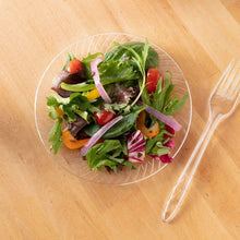 Clear plastic salad plate with leafy greens and sliced vegetables