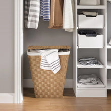 Handwoven laundry hamper in light tan with white liner and folded striped towel on top