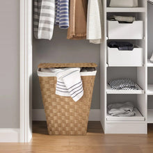 Woven laundry hamper with white liner and striped towels on top, natural tan.