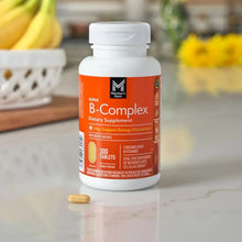 B-Complex dietary supplement bottle with a few yellow tablets on countertop