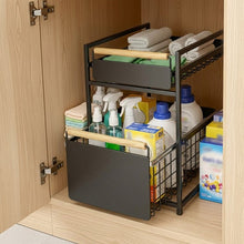 Black two-tier organizer holding towels and cleaning supplies inside a cabinet