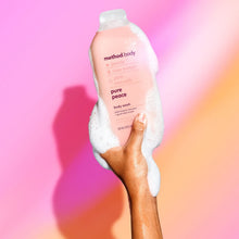 Hand holding pink body wash bottle with pure peace front label