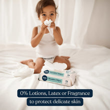 Child holding a wipe to face while sitting with baby wipes pack on bed