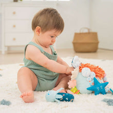 Plush sensory reef toy with dangling sea animals; baby sits on a soft mat