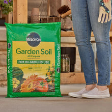 Garden soil bag on floor beside a standing person in jeans and sneakers