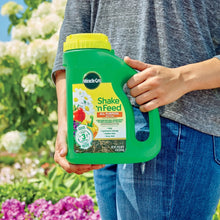 Miracle-Gro Shake n Feed all-purpose plant food bottle held in hands, green jug