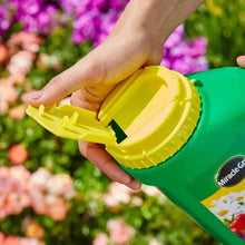 Miracle-Gro Shake 'n Feed jug with open yellow cap, hands tipping and pouring