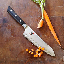 Miyabi Santoku knife with dark handle and light blade, scalloped edge and bolster