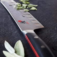 Santoku knife blade close-up with red logo, scalloped edge, and dark handle
