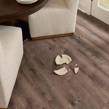 Dark brown wood plank laminate flooring with scattered small white flakes