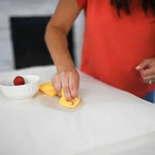 Hand wiping a white tabletop with a yellow cloth