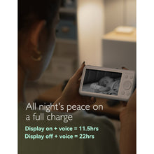 Parent holding baby video monitor at night, screen showing sleeping infant