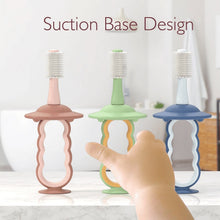 Three suction-base silicone baby toothbrushes in pink, green, and blue handles