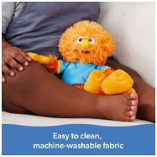 Orange bird plush with blue shirt and yellow beak, resting on a lap on a couch