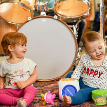 White music cube toy with blue speaker panel, held by toddlers during play