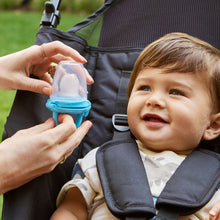 Infant using blue silicone food feeder with spout, held by caregiver