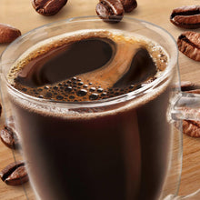 Glass mug of dark coffee with foam, coffee beans around the rim