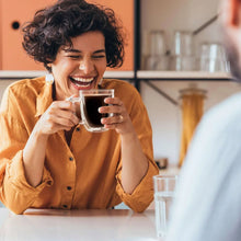 Smiling woman holding a cup of dark coffee on a kitchen counter
