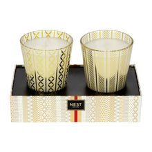 Two patterned candle cups with white wax on a branded candle set tray