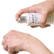 Hand holding and dispensing birch intensive moisture toner from a bottle