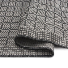 Rolled edge of gray and dark geometric area rug showing thick flat woven pile