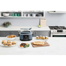 Blue multi-cooker on countertop with serving plates and oven in the background