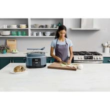 Blue multi-cooker on countertop while a person slices food on a cutting board