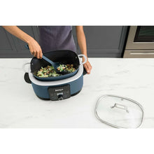 Blue multi-cooker base with inner pot and lid, person lifting the pot