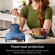 Portable air fryer on countertop with glass container of food and utensil in hand