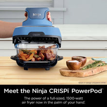 Blue portable air fryer with glass cooking pot filled with roasted meat and vegetables