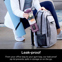 Purple portable blender with clear jar held near a gray bag strap for travel.