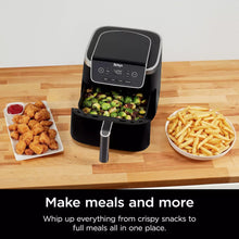 Air fryer on countertop with trays of chicken bites, brussels sprouts, and fries