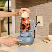 Tumbler blender on countertop as hands lift the lid onto a clear blending cup