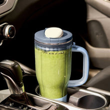 Tumbler blender in a car with a clear cup and green drink, lid closed