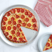 Round pizza pan with a pepperoni pizza slice and whole pizza on a metal tray