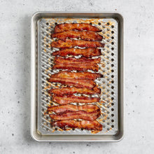 Perforated crisping insert in aluminum roasting pan holding strips of cooked bacon