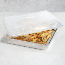 Rectangular aluminum roasting pan with clear lid, holding roasted chicken and vegetables