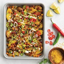 Non-stick baking sheet with roasted vegetables and chicken, garnished with herbs