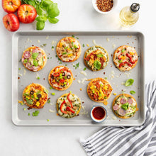 Non-stick baking sheet with pale rim holding mini pizzas with toppings