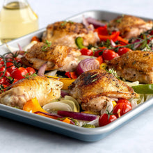 Non-stick baking sheet with blue rim filled with baked chicken and vegetables