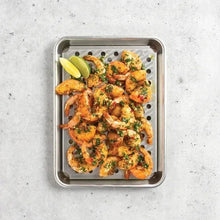 Perforated metal tray with grilled shrimp and herbs on a round-hole surface
