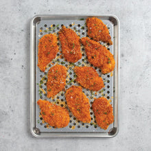 Perforated metal tray with cooked chicken pieces on a round-hole surface