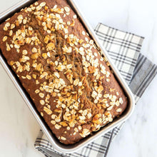 Baked loaf in rectangular metal pan topped with oats and seeds