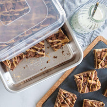 Baked slices in a metal loaf pan with a clear lid, with cake pieces around