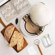 Sourdough loaf with white baking cloche, wooden board, and glass starter jar