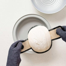 Round dough resting on parchment in a gray pan with dark silicone handles