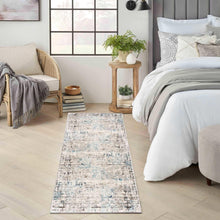 Rectangular area rug with distressed ivory, blue, and gray abstract pattern.