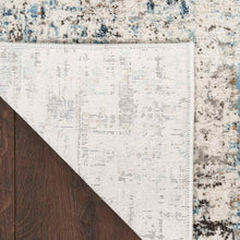 Area rug corner with white backing edge and distressed blue-gray pattern.
